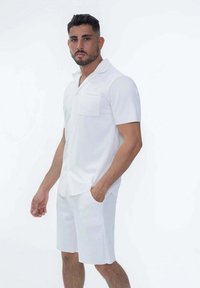 Chemise blanche à manches courtes avec un col en V et une poche, associée à un short blanc cintré. Les deux vêtements présentent une texture subtile.