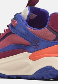 Mehrfarbiger Sportschuh mit einer Mischung aus pinken, blauen und orangefarbenen Materialien; oberer Teil aus strukturiertem Wildleder und Synthetik; Gummisohle mit Traktionsmustern.