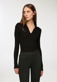 Czarny, prążkowany, długi rękaw polo z dekoltem w kształcie litery V, zestawiony z ciemnozielonymi spodniami w prążki. Gładka tekstura, dopasowany krój.