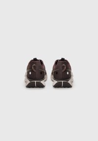 Baskets de sport marron foncé avec tige en textile, semelle extérieure grise claire contrastante et accents réfléchissants. Présentent une languette de traction au niveau du talon.