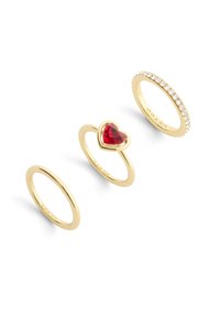 Three gold rings: a plain band, a heart-shaped red stone setting, and a band with clear, set stones along the top edge.