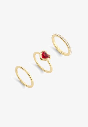 Three gold rings: a plain band, a heart-shaped red stone setting, and a band with clear, set stones along the top edge.