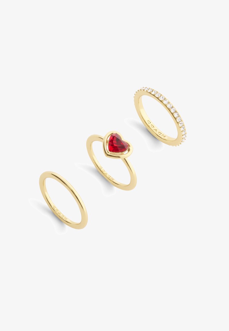 Three gold rings: a plain band, a heart-shaped red stone setting, and a band with clear, set stones along the top edge.