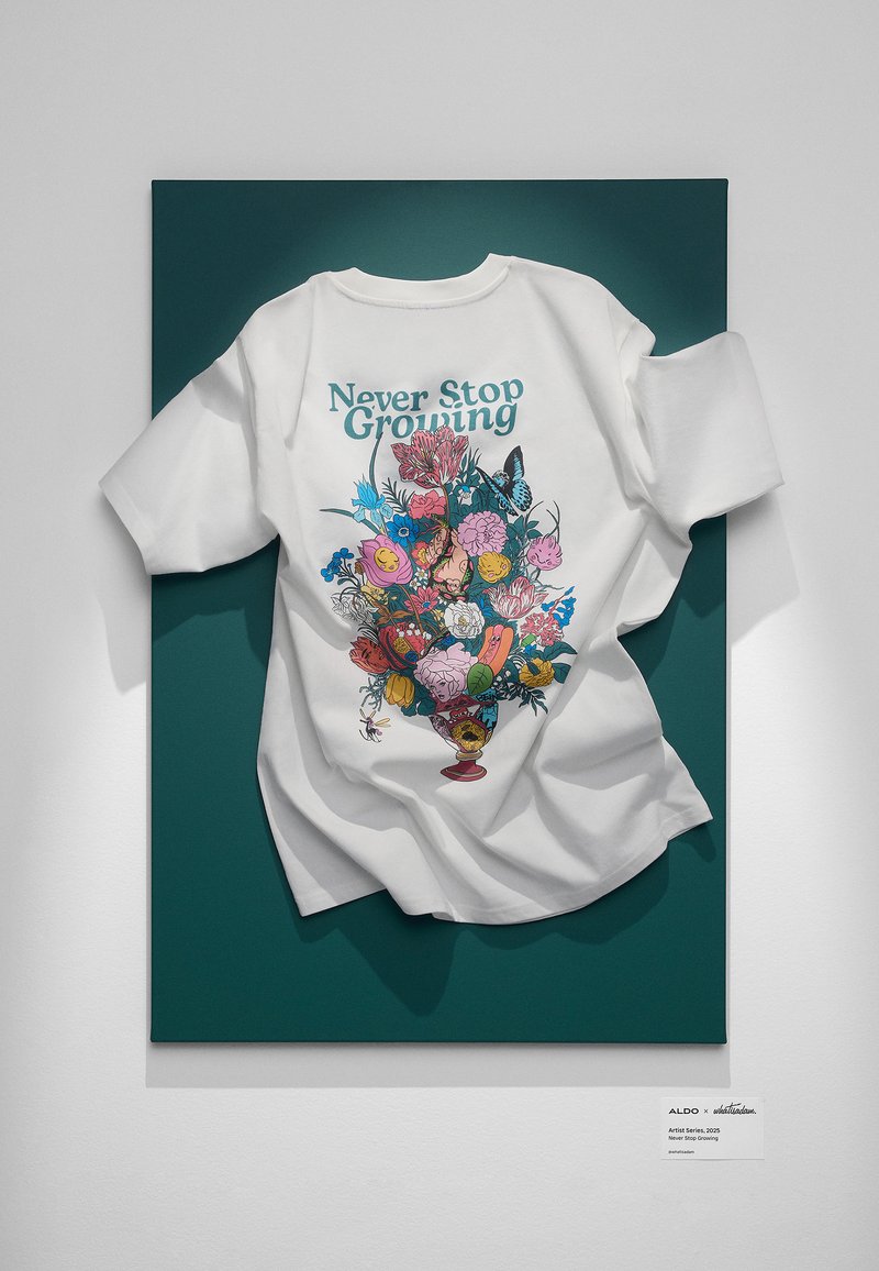 White t-shirt featuring a colorful floral design and the text "Never Stop Growing" on a dark green background. Soft cotton material.