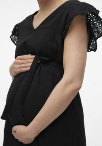 Černé těhotenské šaty s výstřihem do V, krajkovými rukávy, staženým pasem s páskem, strukturovanou tkaninou a splývavým siluetou.