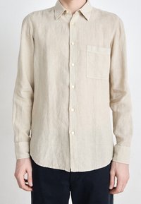 Camicia di lino beige chiaro con maniche lunghe, design con bottoni, colletto a punta e una tasca sul petto. Tessuto liscio, orlo curvo.