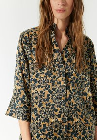 Skjorte med blomsterprint i brun og marineblå, lavet af letvægtsstof. Har krave, halvlange ærmer og detaljerede blomstermønstre.