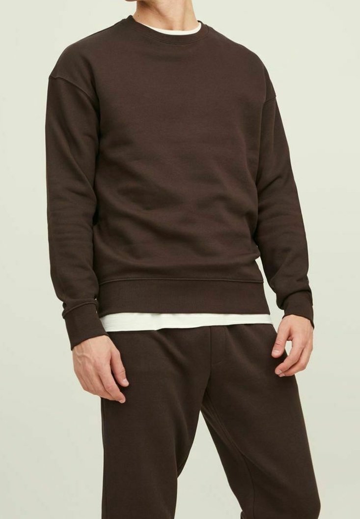 Brun bomullströja med rund halsringning, ribbade ärmslut och nederkant, bärs över en vit skjorta, del av matchande byxor.