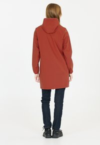 Vedenia, rjave barve dežni plašč s kapuco, elastičnimi manšitami in dolžino do sredine stegna. V kombinaciji z temno denim kavbojkami in črnimi čevlji.