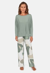 Šviesiai žalia ilgomis rankovėmis palaidinė, atsipalaidavusio silueto, derinama su kreminiais kelnais, kurių didelė abstrakti kamufliažo raštas yra nuosaikiai žalių ir bežinių atspalvių.