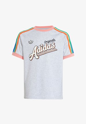 Dwóch młodych ludzi w szarych koszulkach Adidas Originals z różowym obszyciem i tęczowymi paskami na rękawach, w połączeniu z szarymi spodniami na jednolitym tle.