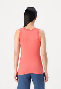 Top de tirantes de color coral con ribetes, bordeado con encaje festoneado en los hombros, diseño ajustado y textura suave. Combinado con pantalones de mezclilla sueltos.