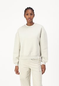 Helles graues Baumwoll-Sweatshirt mit rundem Ausschnitt, überschnittenen Schultern und gerippten Bündchen. Es hat ein dezentes Logo-Tag am Saum.