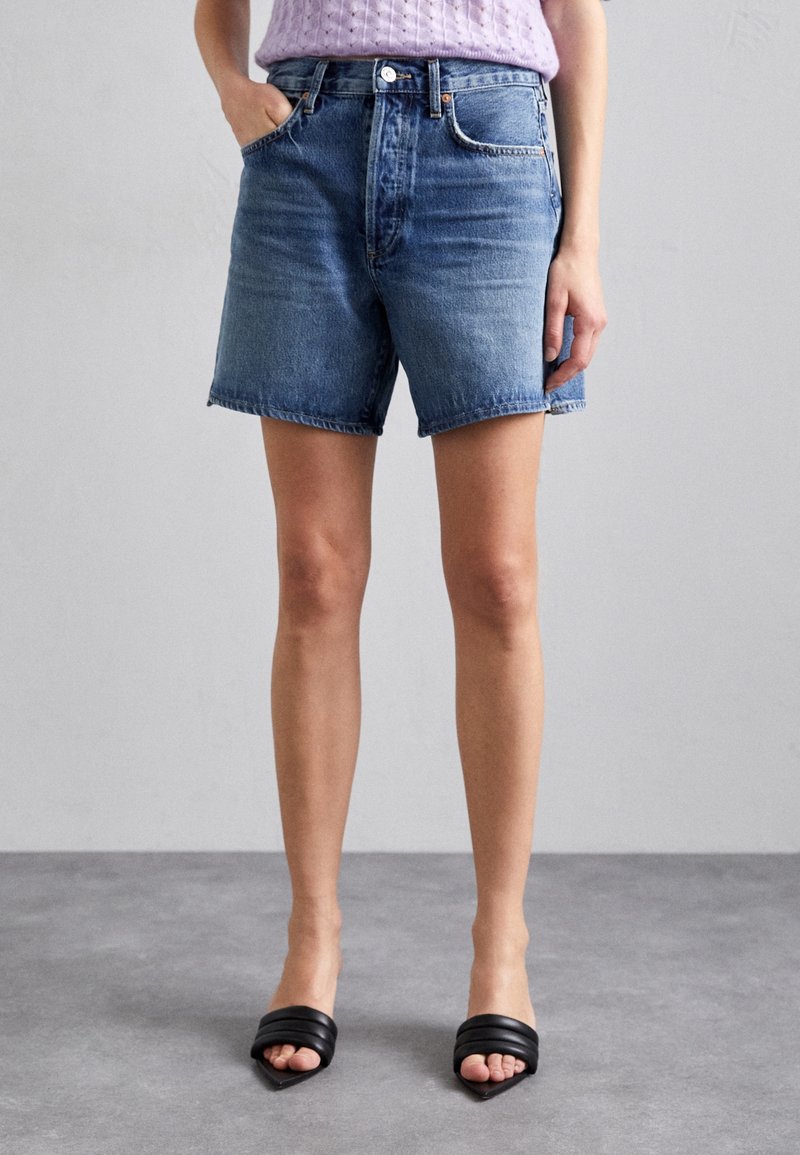 Krótkie spodenki dżinsowe w jasnym niebieskim kolorze, z wysokim stanem i postrzępionym wykończeniem. Posiadają dwie przednie kieszenie oraz klasyczne metalowe detale.