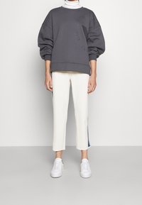 Sudadera gris de gran tamaño con letras texturizadas, combinada con pantalones cremosos de longitud hasta los tobillos con rayas laterales y zapatillas blancas.