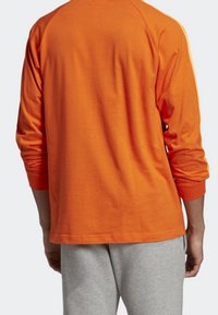 Camiseta de manga larga de algodón naranja brillante con cuello redondo y puños acanalados, que presenta una textura suave y un diseño de mangas raglán.