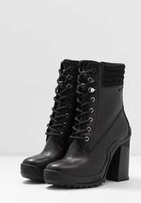 Botas de tobillo negras de cuero suave con un cuello de punto texturizado, cordones en la parte delantera y un tacón grueso y cuadrado con un patrón de suela en zigzag.