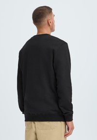 Black sweatshirt with a classic crew neckline, ribbed cuffs and hem, made from soft fabric, worn by a male model, viewed from the back.