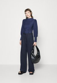Navy blouse with puff sleeves and side ruching, paired with loose navy trousers and a black leather hobo bag. Smooth textures with minimal accents.
