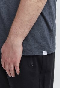 Sötét szürke, rövidujjú póló, puha anyagból készült. Diszkrét fehér címke található az alján. Fekete nadrággal párosítva.