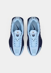 Ein Paar blaue und marinefarbene Nike Shox Sneakers von oben auf einem weißen Hintergrund betrachtet, mit gebundenen Schnürsenkeln und sichtbaren Markenlogos innen und auf den Zungen.