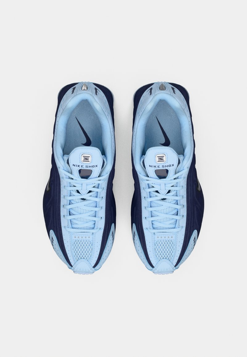 Pareja de zapatillas Nike Shox azul y marino vistas desde arriba sobre un fondo blanco, con los cordones atados y los logotipos de la marca visibles en el interior y en las lenguas.