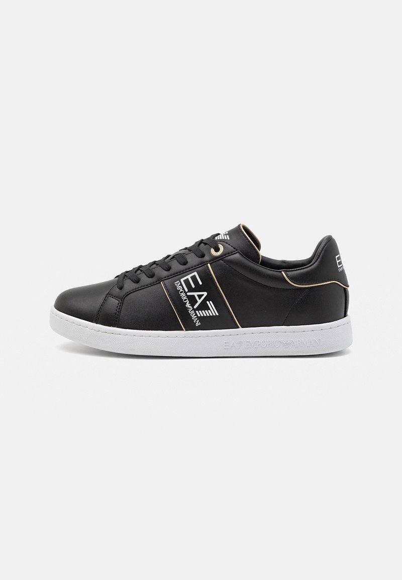 Black leather sneakers with white sole, featuring gold accents and logo. Lace-up design with padded collar for comfort.