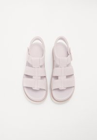 Vaaleanpurppuraiset sandaalit, jotka on valmistettu pehmeästä materiaalista. Niissä on neljä leveää hihnaa, säädettävä solki ja kuvioitu pohja.