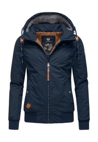 Marineblå yderjakke med hætte foret med uld, brune detaljer og lynlåslukning. Har ribstrikkede manchetter og et logo-patch på siden.