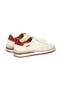 Zapatillas de cuero con parte superior color crema, acentos rojos en el talón y detalles en color marrón claro. Presentan cordones redondos y una suela texturizada.