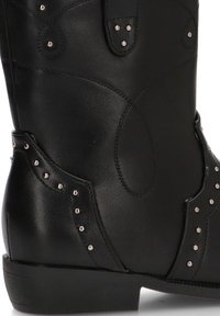 Botas de cuero negro con tacón bajo, tachuelas decorativas de metal y costuras curvas. Textura suave y elementos de diseño clásico del estilo vaquero.
