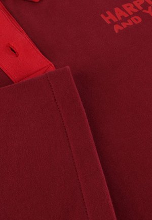 Red cotton polo shirt featuring a ribbed collar and short sleeves. "HAPPY" text printed in a darker red shade on the front. Smooth texture.