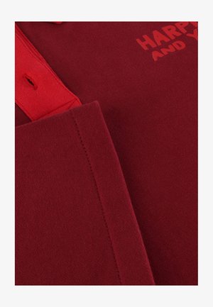 Rotes Baumwoll-Polohemd mit geripptem Kragen und kurzen Ärmeln. Auf der Vorderseite ist der Text "HAPPY" in einem dunkleren Rotton gedruckt. Glatte Textur.