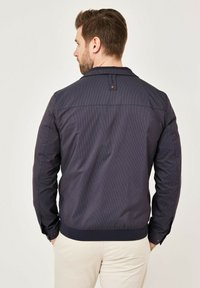 Dark navy bomber jacket with striped pattern, ribbed cuffs, and collar. Features a back tag detail and a smooth, textured fabric.