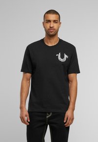 Zwart katoenen T-shirt met korte mouwen en een ronde hals. Bevat een wit logo-graphic op de borst. Eenvoudig, onversierd ontwerp.