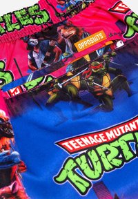 Farebné šortky s korytnačkami Ninja s ružovým a modrým dizajnom, na ktorých sú kreslené postavy, elastický pás a štítok značky.