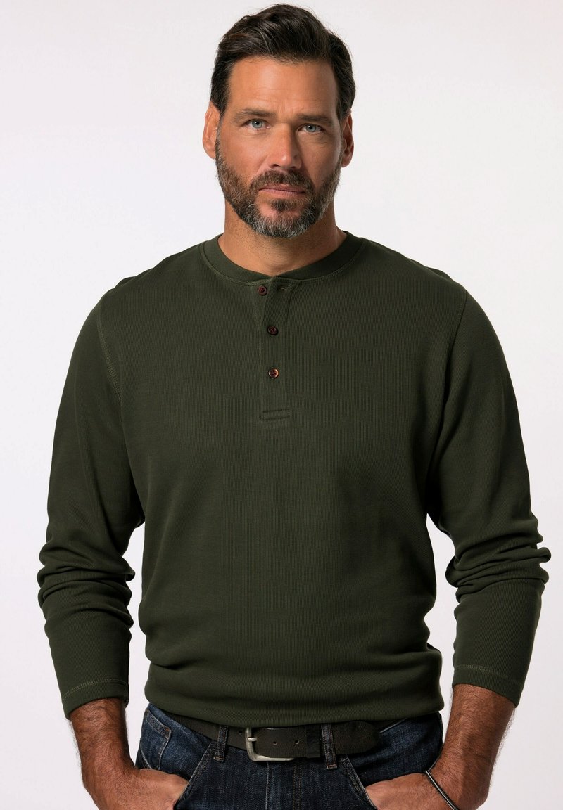 Donkergroene langemouwen henley-shirt met een ronde halslijn, geribbelde textuur en drie bruine knopen op de borst. Gekoeld met blauwe jeans.
