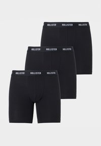 Τρία μαύρα μποξεράκια με λωρίδες μέσης με την επωνυμία «Hollister», τοποθετημένα σε κλιμακωτή στοίβα σε ανοιχτό φόντο.