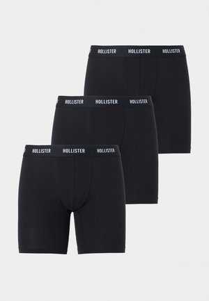 Τρία μαύρα μποξεράκια με λωρίδες μέσης με την επωνυμία «Hollister», τοποθετημένα σε κλιμακωτή στοίβα σε ανοιχτό φόντο.