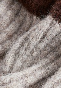 Tissu en laine doux et texturé avec des rayures beiges et marron, montrant des fibres détaillées et un motif de tricot vu de près.