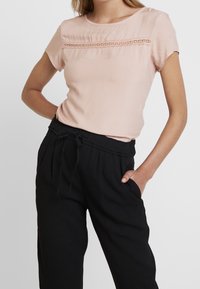 Jasnoróżowa koszula z krótkim rękawem z teksturowanym poziomym wzorem na wysokości klatki piersiowej, połączona z czarnymi spodniami z wysokim stanem i bocznymi kieszeniami.