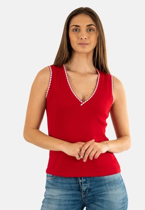 Canottiera rossa a costine con scollatura a V profonda, con bordo bianco lungo il collo e le aperture delle maniche. Abbinata a jeans di denim blu.