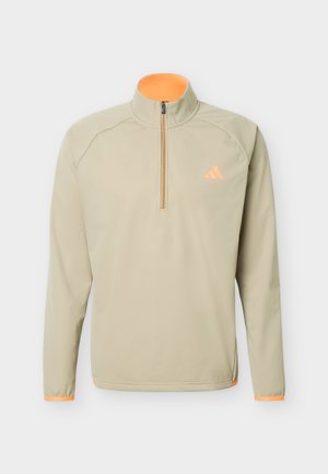 Beige langermet genser med kvartglidelås, høy krage og oransje detaljer på glidelåsen, mansjetter og logo på brystet.