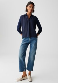 Marineblaue Bluse mit langen Ärmeln und Kragen, kombiniert mit hellblauen weit geschnittenen Jeans und cremefarbenen Loafers, die einen lässigen und entspannten Look zeigen.
