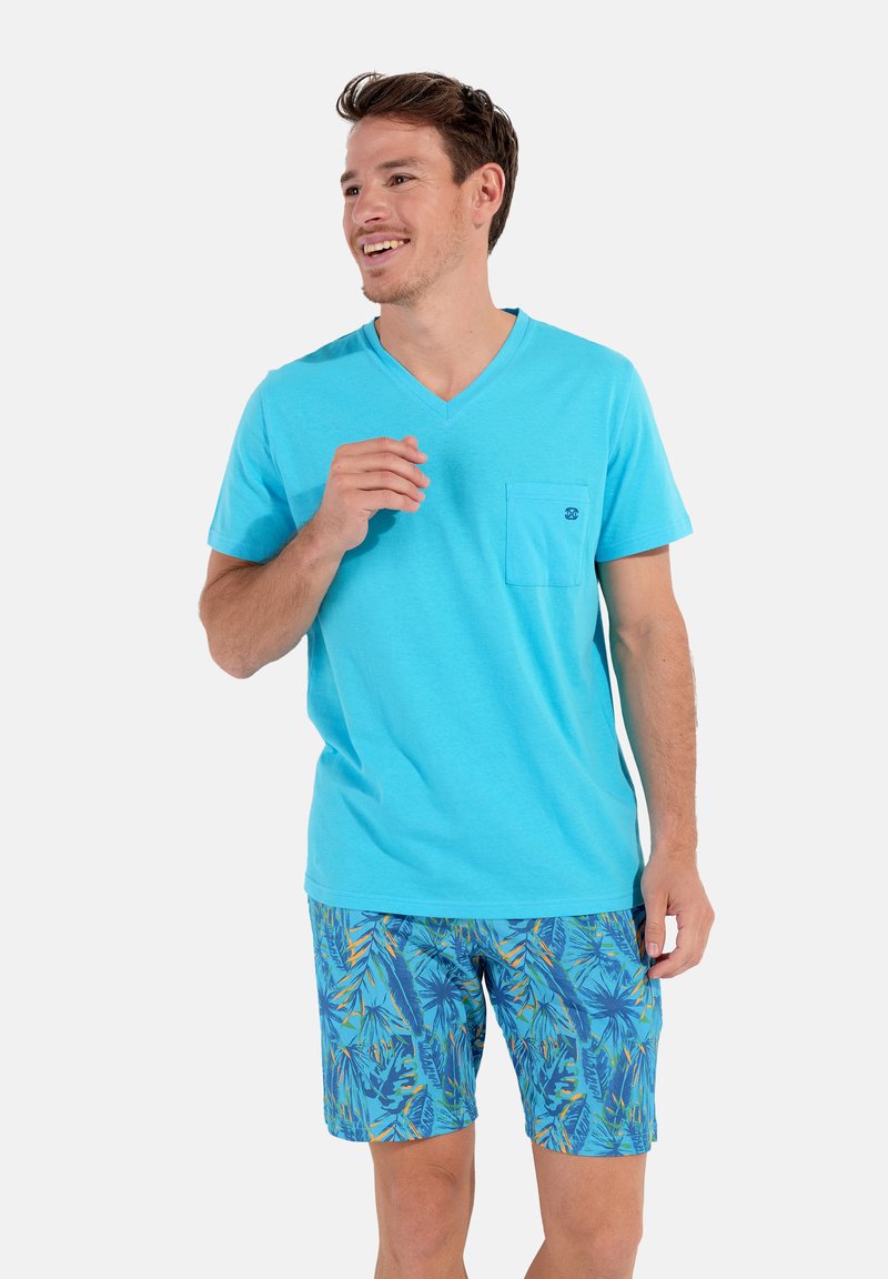 T-shirt turquoise à col en V avec une poche, associé à un short de bain bleu présentant un motif coloré de feuilles tropicales. Fond uni.