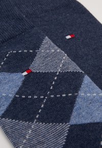 Chaussettes bleu marine avec un motif en argyle dans des tons de bleu et de gris, avec des accents blancs et un petit logo en rouge, blanc et bleu.