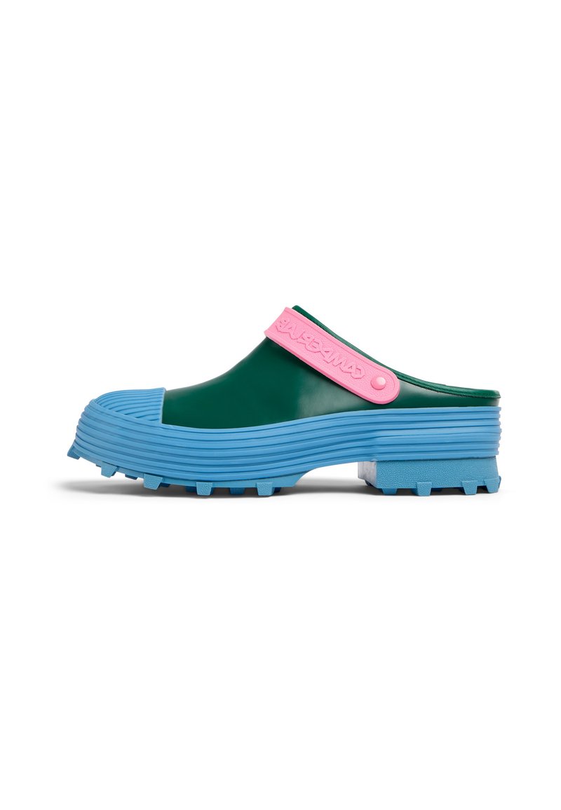 Zoccoli in gomma verdi con suola rigata blu, dotati di una cinghia rosa con marchio impresso. Il design presenta una forma leggermente curva.