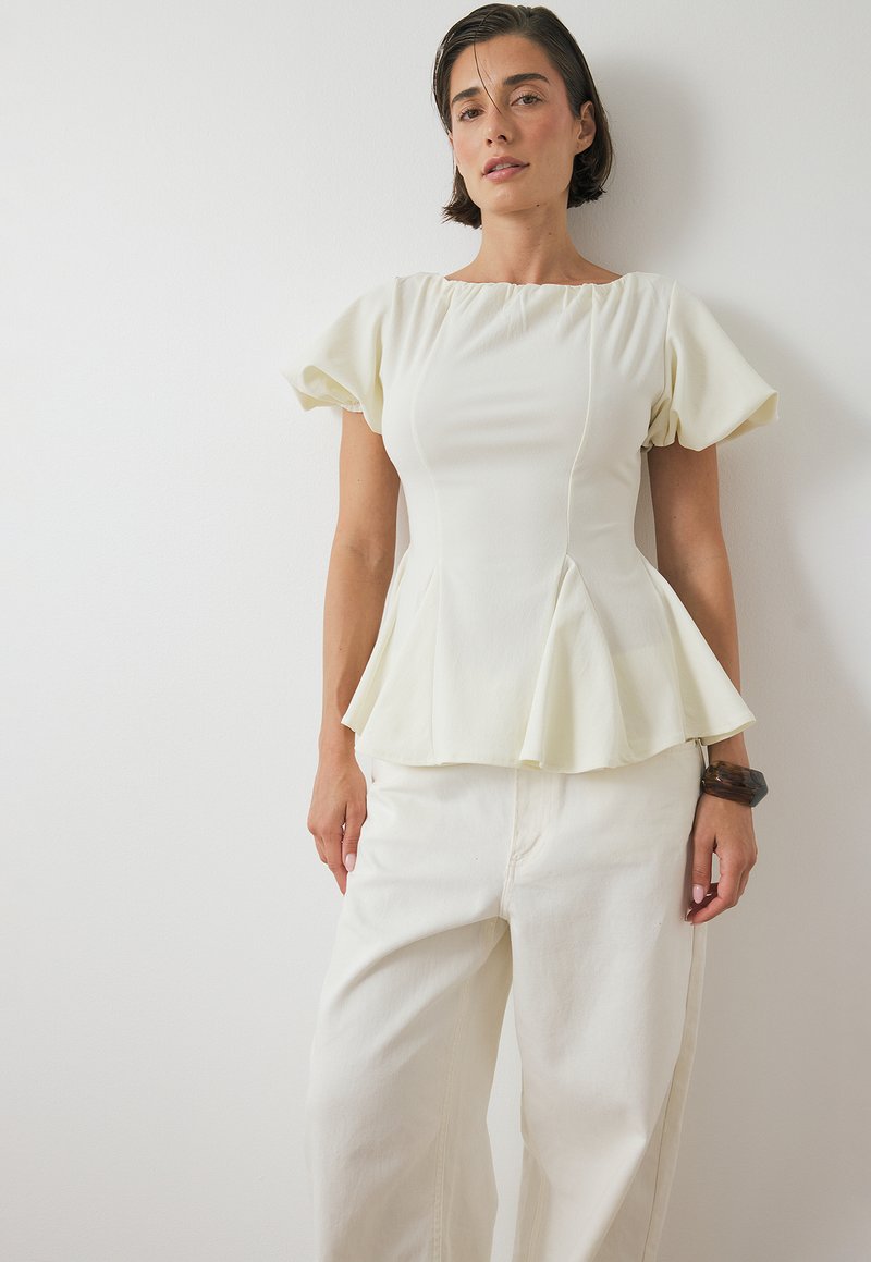 Top bianco a peplo con maniche a sbuffo corte, texture liscia e dettagli lungo le cuciture laterali, abbinato a pantaloni bianchi a vestibilità ampia.