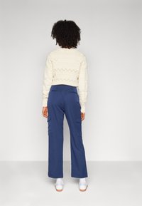 Cream knit sweater with textured patterns, paired with navy cargo pants featuring side pockets and a relaxed fit. White sneakers complete the outfit.