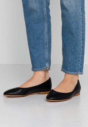 Sorte læderflade sko med spids tå, flad sål og minimalistisk design. Kombination med opfoldede lyseblå jeans.